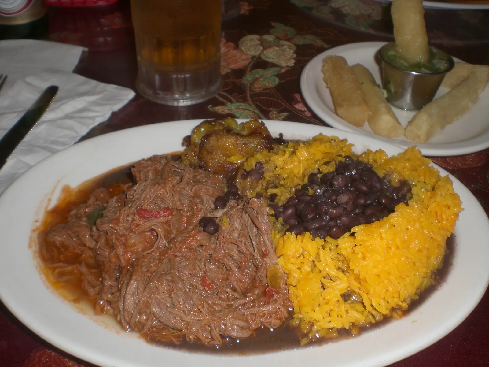 A plate of shredded beef with yellow rice and black beans