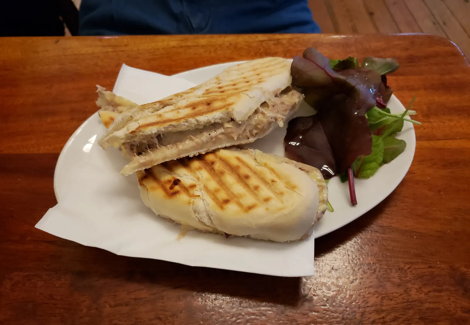 A pressed ham and cheese sandwich cut in half, with salad leaves